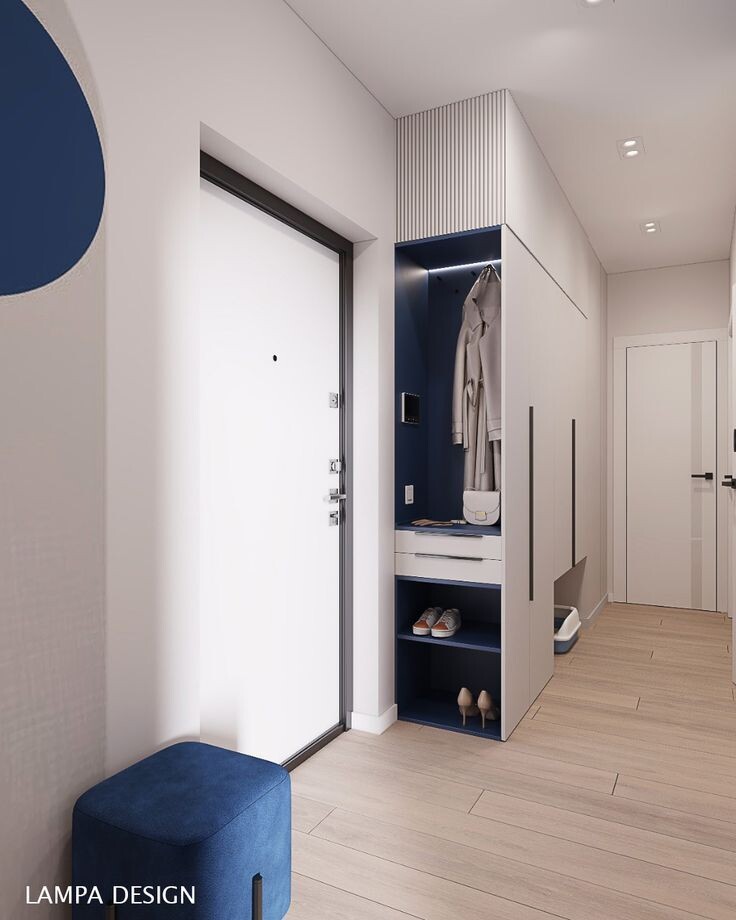Прихожая — это «лицо» квартиры, но часто она становится самым проблемным местом с точки зрения организации пространства. Как разместить верхнюю одежду, обувь, аксессуары и при этом не превратить узкий коридор в загроможденный склад?
Проект от студии LAMPA DESIGN, представленный на фото, — это блестящий пример того, как минимализм, продуманная эргономика и яркий акцент могут решить все задачи маленькой прихожей. Давайте разберем ключевые приемы этого интерьера.
1. Цветовая стратегия: Белый + Дерево + Акцент
Дизайнеры выбрали беспроигрышную комбинацию, которая визуально расширяет пространство:
Белая база: Стены и основные фасады шкафа выполнены в белом цвете. Это «стирает» границы, делая коридор светлее и просторнее.
Натуральное дерево: Светлый ламинат или паркетная доска на полу добавляет теплоты и уюта, смягчая стерильность белого.
Глубокий синий акцент: Чтобы интерьер не выглядел скучным, использован благородный темно-синий цвет. Он повторяется в нише шкафа, на пуфе и в виде геометрического круга на стене. Это связывает композицию воедино и придает ей характер.
2. Зонирование хранения: Принцип «Открытого доступа»
Самая умная часть этого проекта — организация гардеробной зоны у входа.
Открытая ниша: Вместо того чтобы прятать всю одежду за глухими дверями, дизайнеры выделили центральную часть шкафа под открытую зону. Синяя подсветка внутри ниши не только создает уют, но и выполняет практическую функцию — подсвечивает вещи.
Сценарий «Пришел домой»: В нише есть крючок для куртки, полка для сумки и ключей, а также удобный ящик для мелочей (перчатки, шарфы). Это позволяет разгрузиться сразу при входе, не открывая шкафы.
Обувница: В нижней части ниши расположены открытые полки для повседневной обуви. Это гигиенично (обувь проветривается) и удобно.
3. Скрытые решения: Место для питомца
 📍 Приходите знакомиться:
г. Омск, ул. Фрунзе 1/4, ТЦ «Миллениум», 11 этаж
📞 Звоните или пишите: +7 (3812) 99-20-38