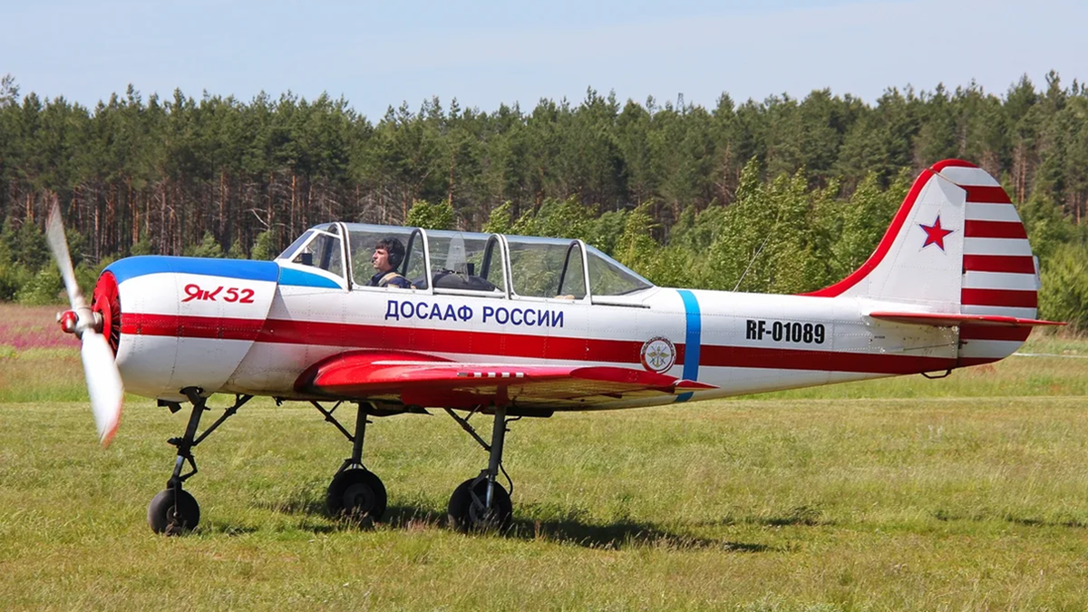 На фотографии: Як-52 – винтовой легкомоторный учебно-тренировочный самолёт (УТС), первый полет состоялся в 1976 году, КБ "Яковлева". ДОСААФ России. Источник фото: https://avatars.mds.yandex.net/i?id=eeb85ade5006ceae56292748fe2ed486_l-5234751-images-thumbs&n=13