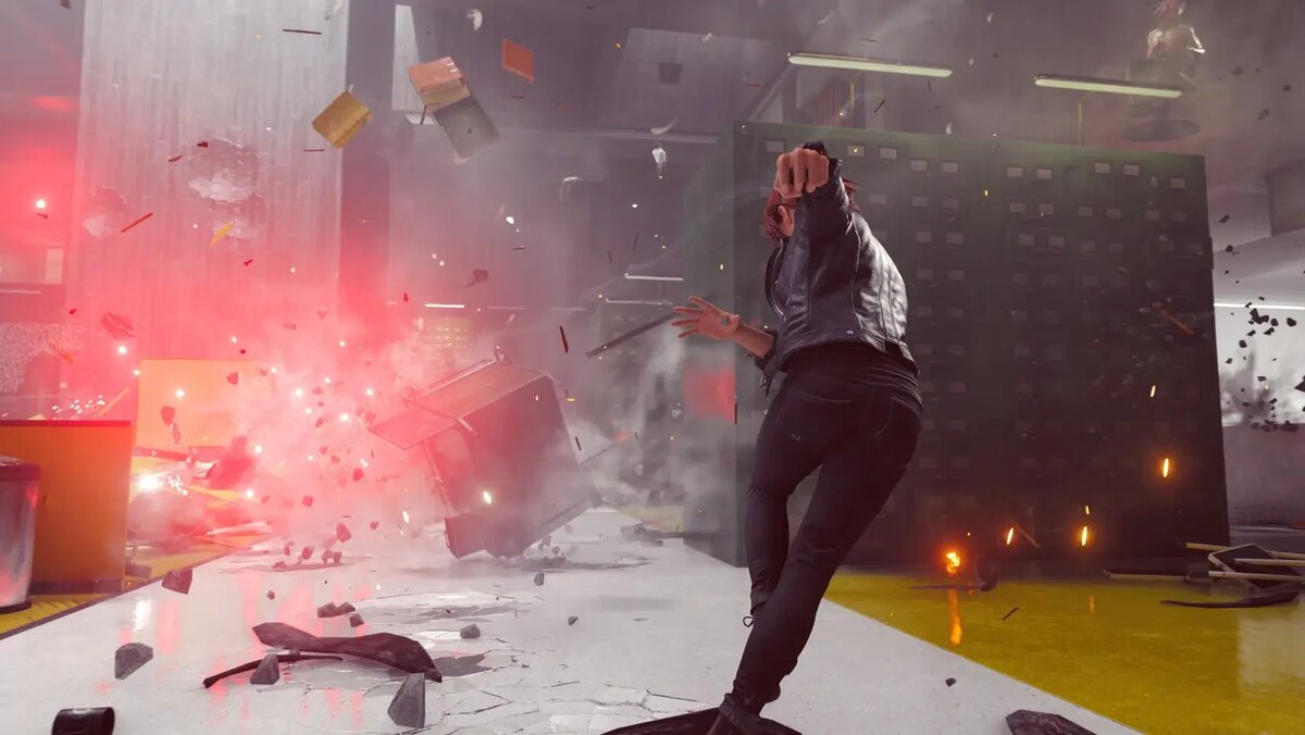    Person in a leather jacket dodges debris as a red explosion erupts in a warehouse-like room with flying objects around.