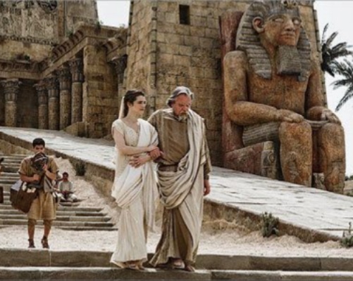 Кадр из фильма «Агора» (2009, реж. Алехандро Аменабар. Стены домов покрыты следами времени: сколы штукатурки, пятна сырости, мох в швах кладки. Фрагменты разрушенных колонн и статуй, частично занесённые пылью