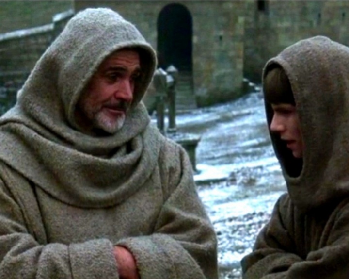 Кадр из фильма «Имя розы» (реж. Жан-Жак Анно, 1986). Массивные каменные стены покрыты тёмными вертикальными потёками от дождей и зеленоватым налётом мха. Земля во дворе — сырая, тёмно-коричневая глина, в которой видны глубокие следы от монашеских сандалий