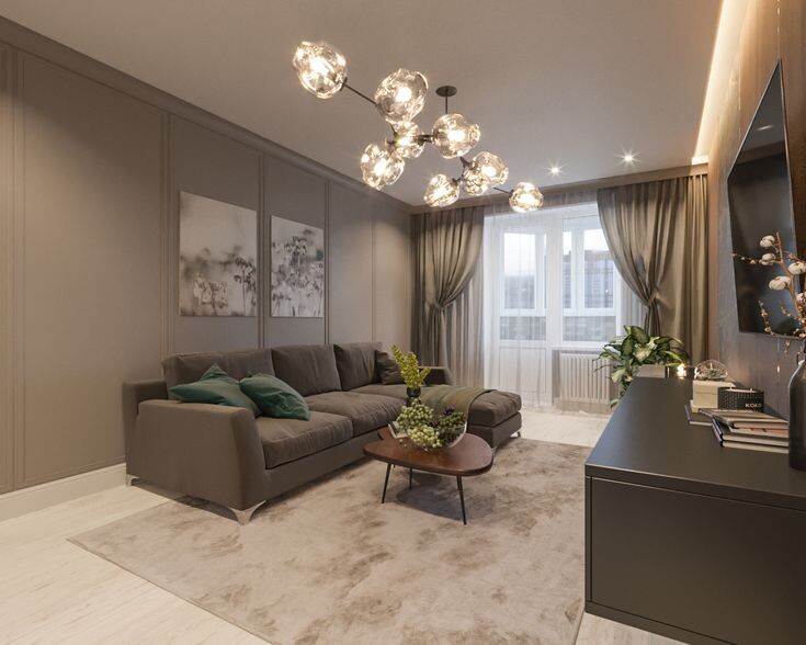 На фотографии представлен интерьер гостиной, который можно назвать эталоном современной элегантности. Это пространство, где нет кричащих цветов или лишних деталей, но есть ощущение безупречного вкуса, спокойствия и дорогого уюта. Дизайнер мастерски использовал монохромную палитру, игру фактур и акцентное освещение, чтобы создать комнату, в которой хочется задержаться надолго.
Давайте разберем ключевые приемы этого дизайна и узнаем, как создать подобную атмосферу «тихой роскоши» в своей квартире.
1. Цветовая палитра: Сила нейтралов
Основа интерьера — сложная гамма оттенков тауп (taupe). Это цвет, находящийся на стыке серого и бежевого.
Почему это работает: В отличие от чистого серого, который может казаться холодным, или бежевого, который иногда выглядит старомодно, тауп обладает благородной глубиной. Он создает «обволакивающий» эффект, делая комнату визуально просторной, но при этом уютной.
Монохром: Стены, шторы, диван и ковер выдержаны в близких тонах. Это стирает границы между предметами и создает ощущение единого воздушного пространства.
Акценты: Чтобы интерьер не стал скучным, добавлены глубокие изумрудно-зеленые подушки и живые растения. Этот природный цвет освежает палитру и добавляет жизни.
2. Архитектура и текстуры: Объем без лишних стен
Чтобы монохромный интерьер не выглядел плоским, дизайнер добавил рельеф и фактуру.
Стеновые панели (молдинги): Обратите внимание на стену за диваном. Классические прямоугольные панели (буазери) придают комнате архитектурность и статусность. Они разбивают большую плоскость стены, добавляя тени и объема.
Текстиль: Массивный диван с мягкой обивкой (вероятно, велюр или рогожка) контрастирует с гладкими стенами.
Ковер: Большой ковер с размытым рисунком (под мрамор или облака) зонирует гостиную зону. Его светлый оттенок перекликается с полом, но более пушистая текстура добавляет тактильности.
📍 Приходите знакомиться:
г. Омск, ул. Фрунзе 1/4, ТЦ «Миллениум», 11 этаж
📞 Звоните или пишите: +7 (3812) 99-20-38
 