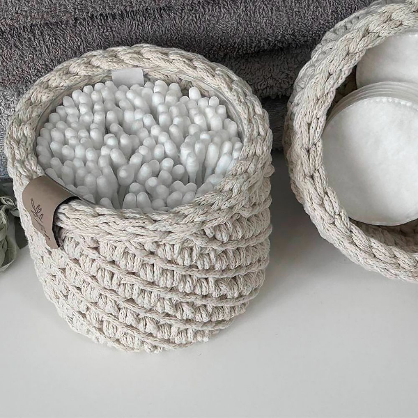 Пластиковая баночка с ватными палочками не спрятана в ящик — она «одета» в вязаную корзину. Рядом — корзина с ватными дисками. Никакого визуального шума, только уют и порядок на полке в ванной.