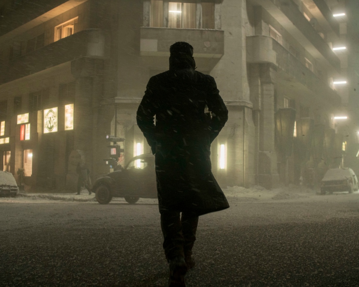 Кадр из фильма «Бегущий по лезвию 2049» (реж. Дени Вильнёв, 2017) Посмотрите на этот кадр: широкая улица антиутопичного Лос-Анджелеса. Огромные бетонные здания подавляют своими масштабами, их стены покрыты многослойными разводами серой грязи — вертикальными потёками, оставленными десятилетиями непрекращающихся осадков. В воздухе висит густая смесь тумана и смога, оседающая влагой на ржавых конструкциях. Этот кадр — ключ к пониманию замысла Гасснера и Вильнёва: город не просто выглядит грязным, он пропитан влагой насквозь, бетон и сталь впитали десятилетия упадка.