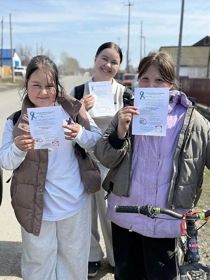 Три девушки держат буклеты «Синяя лента апреля»