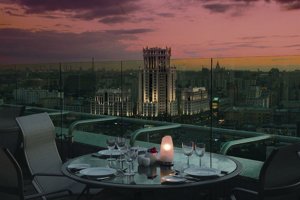 Панорамный вид на вечернюю Москву с террасы отеля Swissôtel Красные Холмы 5* на Космодамианской набережной, 52с6. Отель расположен в одном из самых высоких зданий столицы в районе Замоскворечья. В 2026 году это место остается лучшей локацией для романтического ужина с обзором 360 градусов, где огни города и вид на высотку на Котельнической набережной создают неповторимую атмосферу.