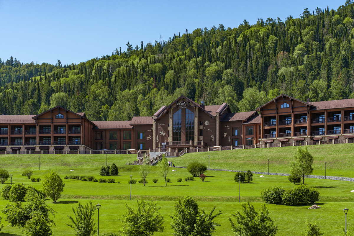 Панорамный вид на архитектурный ансамбль Cosmos Collection Altay Resort 5* в селе Урлу-Аспак на улице Лесхозная, 20. Отель расположен в уединенной долине среди хвойных лесов Майминского района Республики Алтай. В 2026 году этот комплекс на ровном, благоустроенном рельефе остается эталоном премиального отдыха, предлагая гостям безупречный сервис, собственный центр восстановительной медицины и атмосферу абсолютного спокойствия в окружении гор.