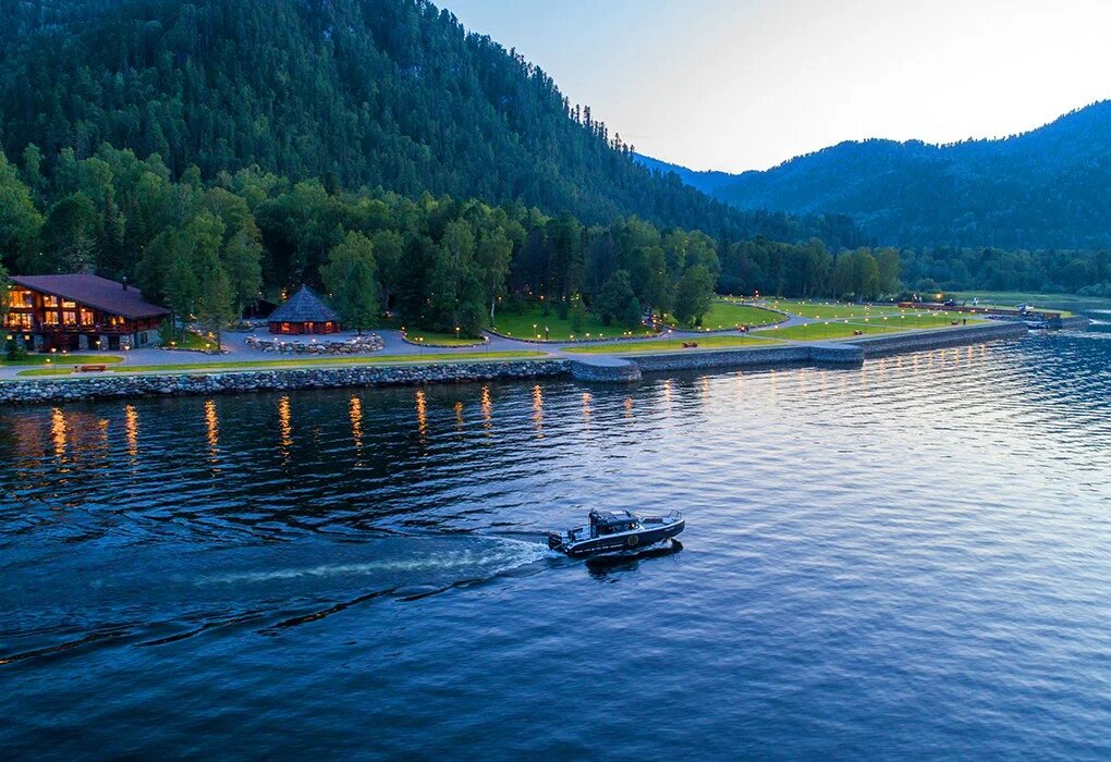 Панорамный вид на набережную Altay Village Teletskoe 5* в урочище Кордон Самыш, 1. Этот эксклюзивный курорт расположен на первой береговой линии Телецкого озера в окружении нетронутой алтайской тайги. В 2026 году отель на абсолютно ровном и благоустроенном рельефе побережья остается эталоном уединенного отдыха, предлагая гостям приватные шале из кедра, собственный флот для прогулок по озеру и вертолетные экскурсии.