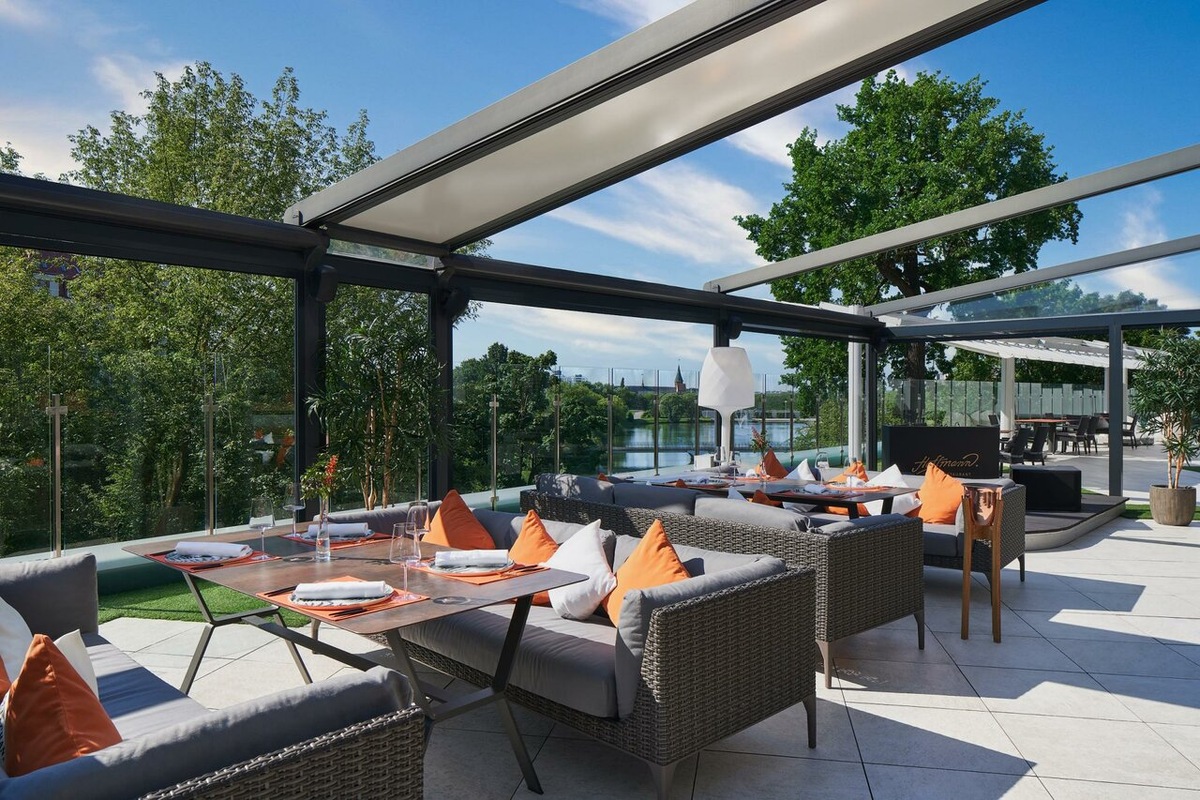 Летняя терраса ресторана Hoffmann в отеле Crystal House Suite Hotel & SPA 5* в Калининграде по адресу улица Сергеева, 4. Пространство с панорамным остеклением и видом на Нижнее озеро спроектировано для комфортного отдыха на открытом воздухе с сохранением высокого уровня сервиса. В 2026 году это актуальная локация для завтраков и деловых встреч в историческом центре города с доступом к премиальной гастрономии.
