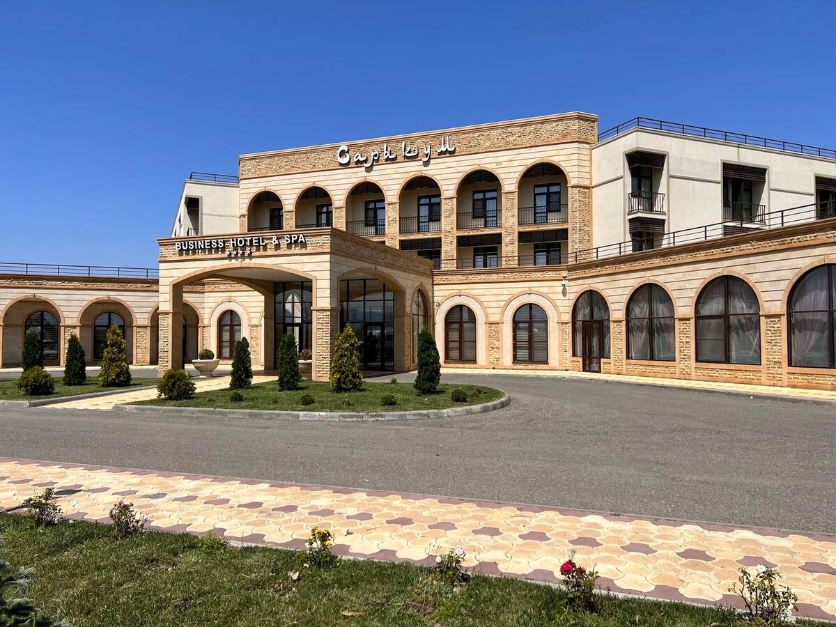 Фасад Сарыкум Business Hotel & SPA 4* на улице Ислама Исракова, 300 в селе Коркмаскала. Отель расположен в непосредственной близости от уникального природного памятника — бархана Сарыкум, и располагает современным спа-центром с крытым бассейном и хаммамом. В 2026 году этот объект остается востребованным для планирования отдыха благодаря возможности совместить посещение заповедных локаций Дагестана с высоким уровнем гостиничного сервиса.