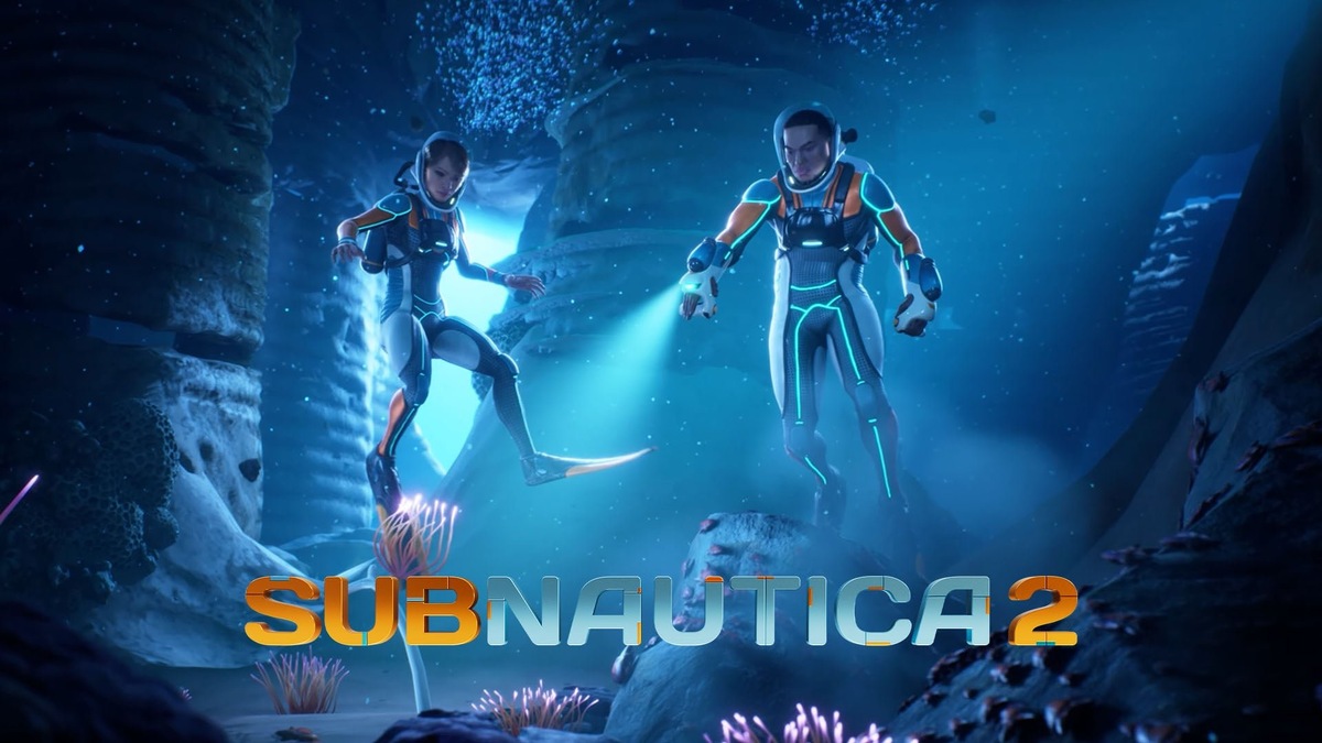    Two divers in glowing orange-and-blue suits hover in an underwater cavern, with the Subnautica 2 logo at the bottom.