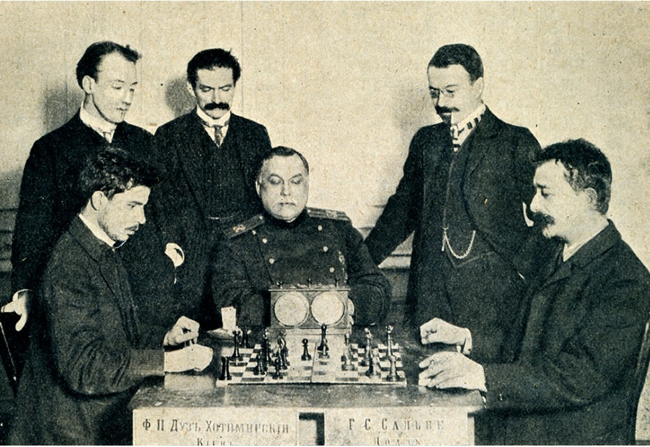 Петербург, 1909, турнир памяти Михаила Чигорина. За партией Георг Генрих Сальве – Фёдор Дуз-Хотимирский (на фото слева) наблюдают (слева направо) члены турнирного комитета В.Чудовский и Ю.Сосницкий, председатель Лодзинского общества любителей шахматной игры К.Манакин и мастер А.Левин.  Фото из турнирного сборника
