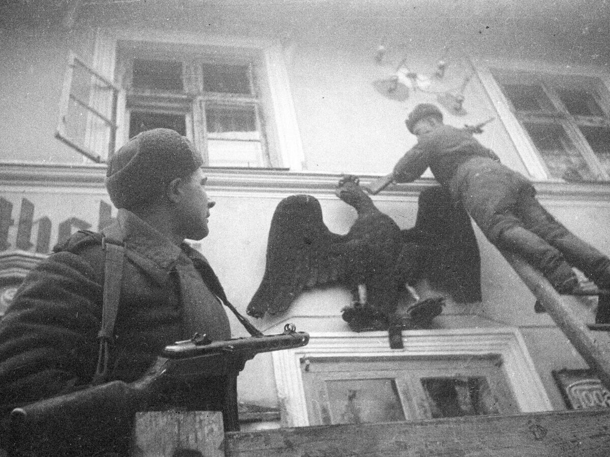    Советские солдаты сбивают нацистскую символику с фронтона здания в освобожденном городе Меденау (ныне Логвино). | © РИА Новости / Николай Максимов