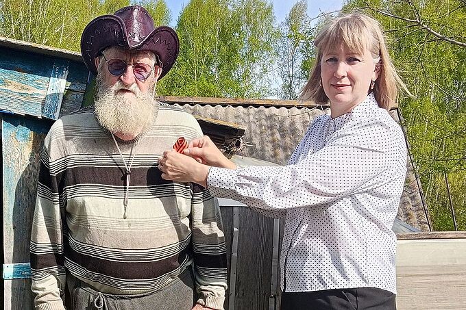 Социальный работник прикалывает Георгиевскую ленточку пожилому мужчине