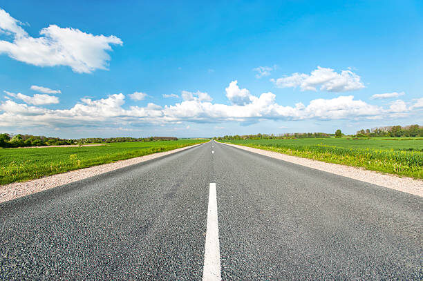    Asphalt road in green fields on blue cloudy sky background. Multicolored vibrant outdoors horizontal image. Алена Гончаренко
