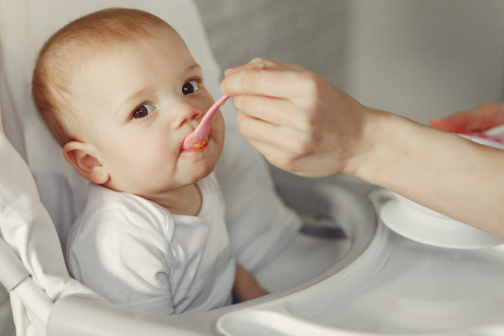    Baby eating. Mother feeds the baby. Little child in a kid's chair. redaktor