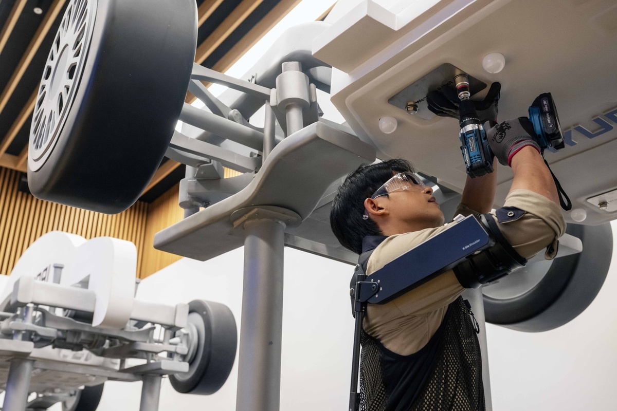 Исследователь из Robotics Lab, надевший робота «X-ble Shoulder», который поддерживает силу мышц плеча, поднимает руку, чтобы закрепить деталь в нижней части макета автомобиля [Предоставлено Hyundai Motor Group]
