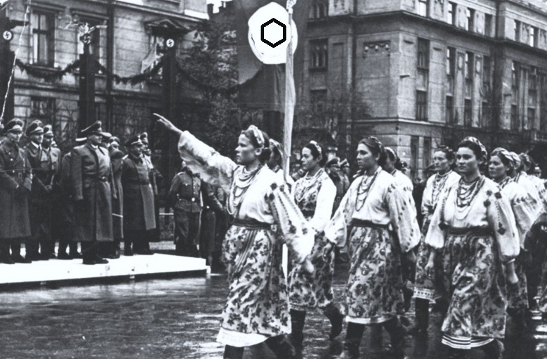 Парад в городе Станислав (ныне - Ивано-Франковск) в октябре 1941 года. Из идейных и нравственных соображений изображение на флаге замазано в фоторедакторе белой краской и вместо него нарисован другой, "безобидный" символ. 