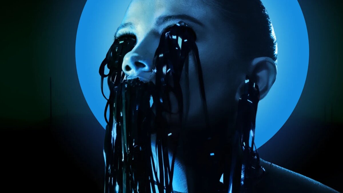    Close-up of a person with black strips hanging over the face, backlit by a blue circular light behind.