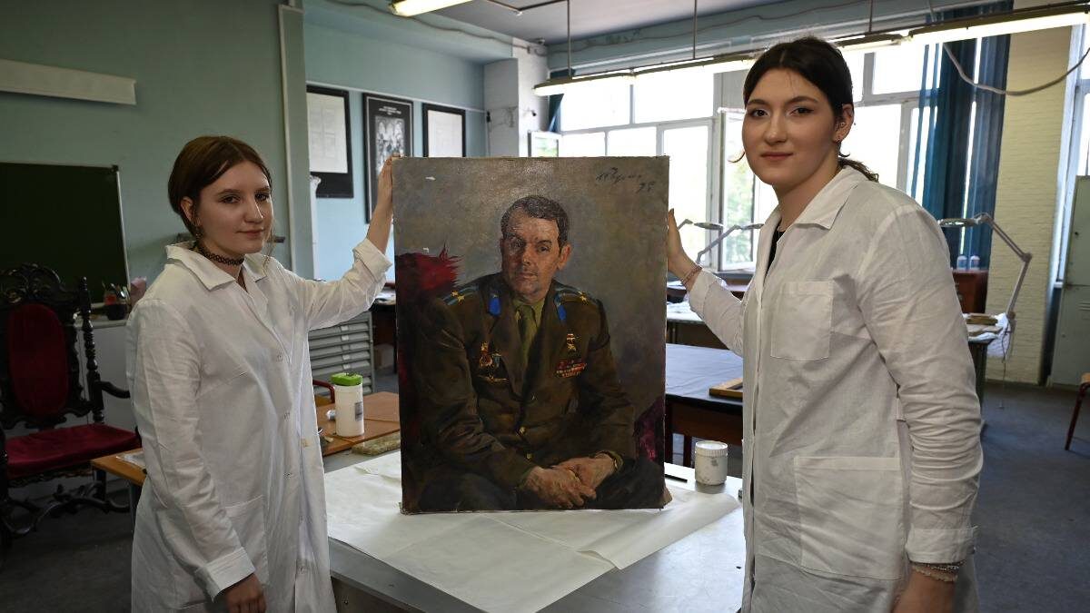    Студентки колледжа «26 КАДР» Настя Воронова и Арина Карпова показывают реставрируемый экспонат — портрет «Ветеран Войны Н. Е. Воробьев» 1975 года художника Игоря Радомана / Фото: Анатолий Цымбалюк / Вечерняя Москва