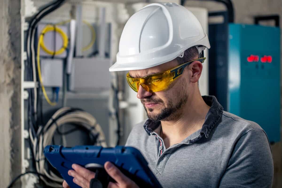    Man, an electrical technician working in a switchboard with fuses. Installation and connection of electrical equipment. Professional uses a tablet. Фелор Круглов