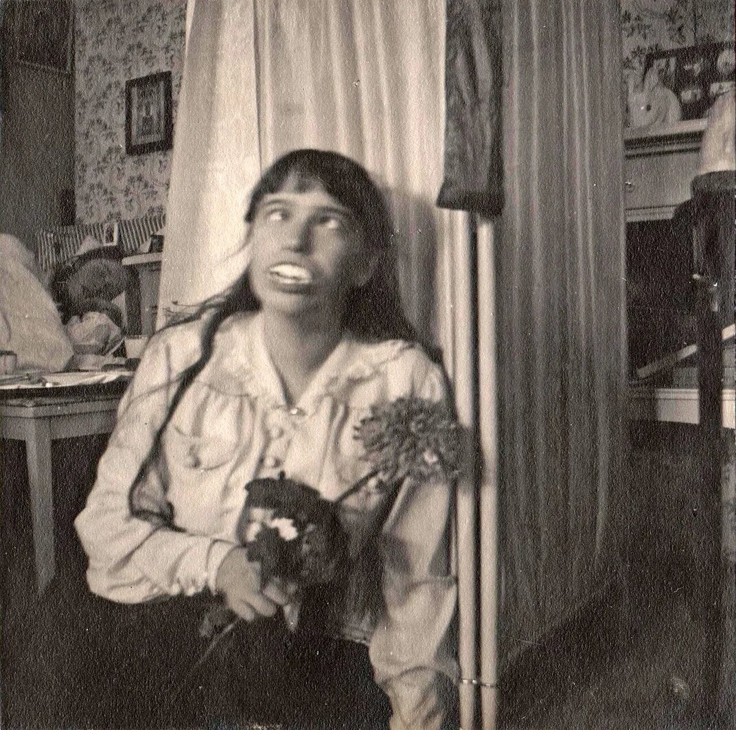 Анастасия носит вставные зубы. На заднем плане спит её сестра Ольга. Общественное достояние, доступно через Wikimedia Commons.
