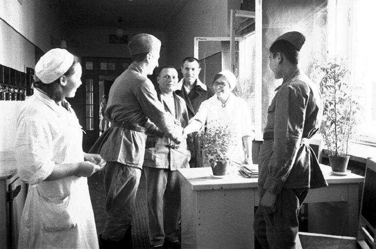 Фотография сделана в стенах Красноярского пединститута в годы войны, когда там располагался эвакогоспиталь № 1350. Герои фото и точная дата снимка неизвестны. Вероятно, фотограф успел «поймать» момент выписки пациентов, благодарящих медиков