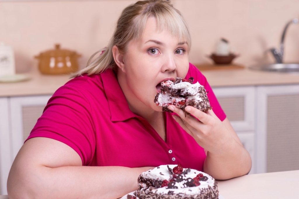 Young overweight woman eating big piece of cake
