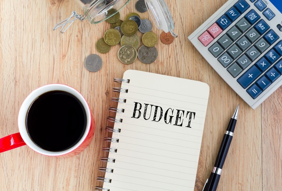 Budget text on notepad — coffee, coins,pen and calculator on top of wooden table.