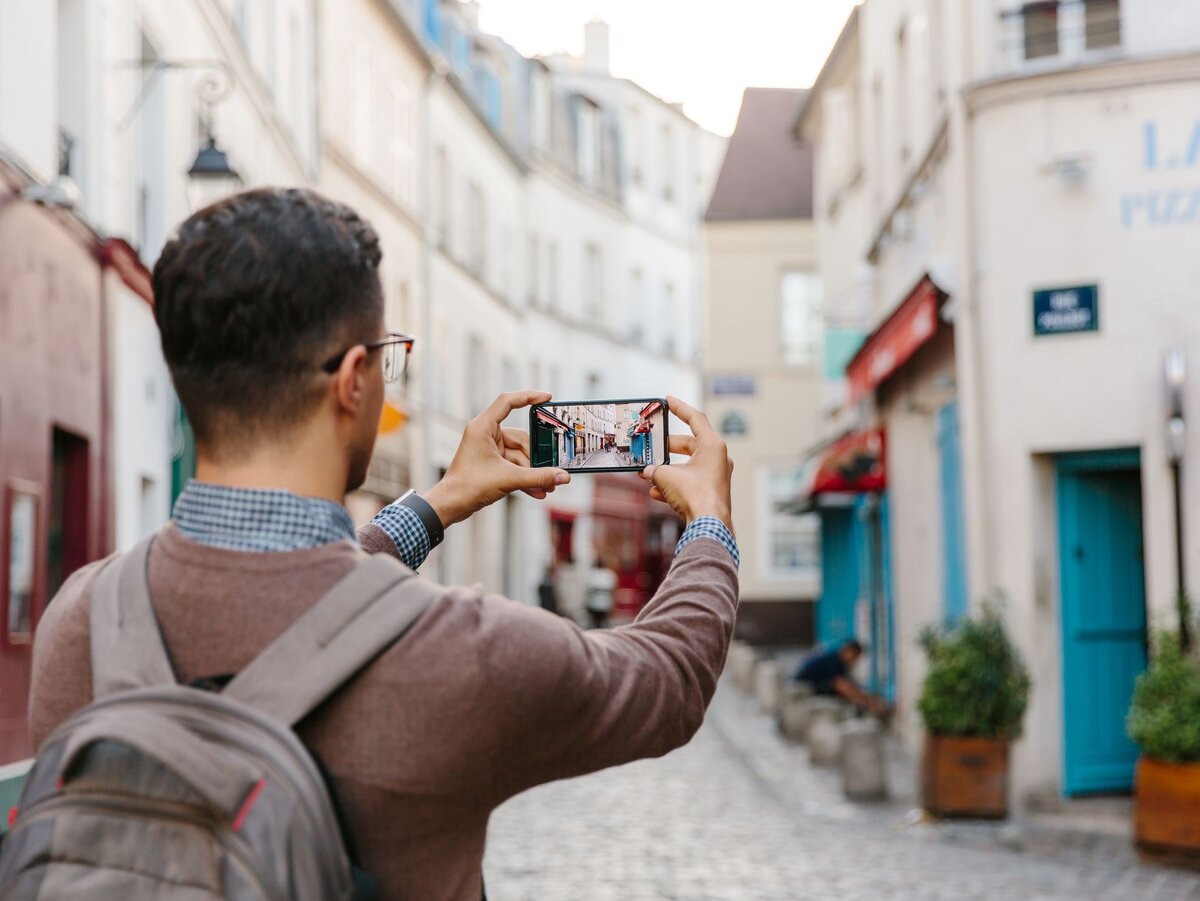 Tourist with Phone. Снимает на смартфон улочка. Boy with Phone. Город в котором нельзя фотографировать.