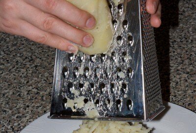 Возьмите большую плоскую тарелку, натрите отварной картофель на крупных слотах терки первым слоем сразу на тарелку и равномерно распределите по ней.