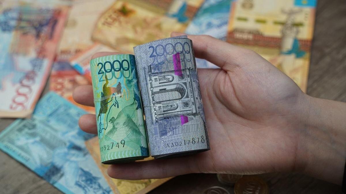    Человек держит в руке тенге:NUR.KZ / Владимир Третьяков