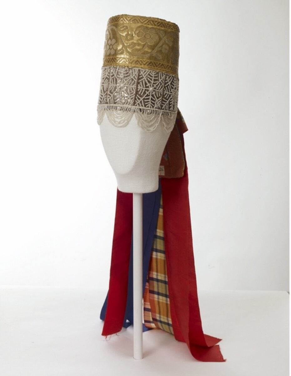 Повязка - высокий праздничный головной убор в форме цилиндра.
Описание предмета. (Перевод с финского языка):

"Повязка" девичья: твердая бумага с пришитой красной подкладкой и переплетом с золотой  лентой вверху и серебряной бумагой (ред. обычно фольга) с жемчугом внизу; разноцветные шелковые ленты свисают со спины.

Головной убор девушки высокий, укреплен фольгой или картоном. Головной убор обтянут серебристой бумагой, на которую нашито сетчатое украшение из мелких стеклянных бусин. С нижнего края головного убора изогнуто свисают нити из таких же бусин. К верхней части головного убора пришита широкая лента из золотых нитей с цветочно-лиственным мотивом. Головной убор затягивается на голове двумя тканевыми лентами синего цвета. На шее можно завязать большой бант, который завязывается из широкой красной шелковой ленты.

Украшение: жемчужное украшение

Национальный музей Финляндии

Измерения
высота: 24,0 см
диаметр: 18,0 см
длина, самая большая, декоративные полосы: 63,0 см

Время изготовления до 1911 года
Техника: ручная работа
Техника: рукоделие_текстиль/шитье
Техника: ручная работа_текстиль/нарезание резьбы
декоративные ленты: Техника: рукоделие_текстиль/шитье
Материал: ткань/парча
Материал: ткань/шелк
Материал: жемчуг/стекло
Материал: декоративные ленты: ткань/шелк
основной материал: картон
Россия, Архангельск, Петрогорская

Праздничный головной убор для девушки. Волосы заплетены в одну косу, а на голове повязана красная шелковая лента.
