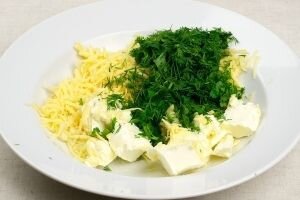     Сыр нужно измельчить на крупной терке. Зелень укропа и петрушки тщательно промываем и просушиваем. Ножом шинкуем зелень мелко и добавляем в миску к натертому сыру. С долек чеснока снимаем шелуху, промываем их и пропускаем через специальный пресс. Добавляем в миску. Туда же отправляем нарезанное на крупные кубики сливочное масло. Все ингредиенты нужно хорошо перемешать до однородного состояния.   