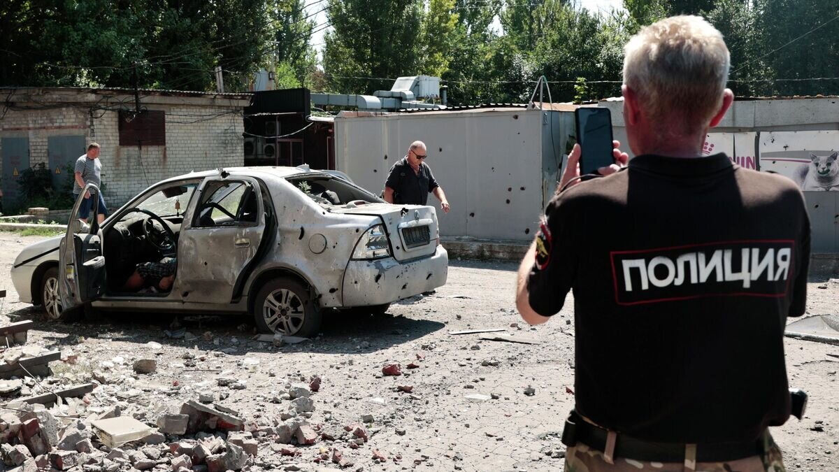    Сотрудник полиции у автомобиля после обстрела ВСУ в Кировском районе Донецка© РИА Новости / Сергей Аверин