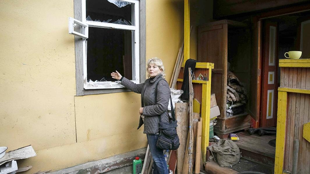 Местная жительница показывает окно, разбитое в результате взрывов на военном складе. Фото: REUTERS/Gleb Garanich