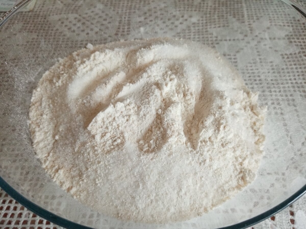 В просеянную муку всыпать соль, сахар, сухие дрожжи и хорошо перемешать, чтобы ингредиенты равномерно распределились.