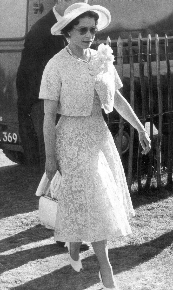 Королева Елизавета II по пути на коктейльную вечеринку в 1959 году. На ней лимонный кружевной костюм, широкополая шляпа и солнечные очки. Ее пышная юбка и короткий жакет отражают модный силуэт 1950-х годов.