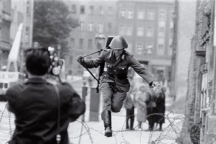 На фотографии, сделанной спустя 28 лет, когда Берлинская стена доживала свои последние часы как граница между двумя Германиями, молодые восточногерманские военные — ровесники Шумана в день его побега — смотрят на протянутую им жителем Западного Берлина руку с настороженностью. 
Тогда, 9 ноября 1989 года, пограничники, полицейские и солдаты армии ГДР не стали препятствовать стремлению своих сограждан попасть на Запад. Все ответственные за Стену службы работали, соблюдая немецкий порядок и даже проявляя доброжелательность.