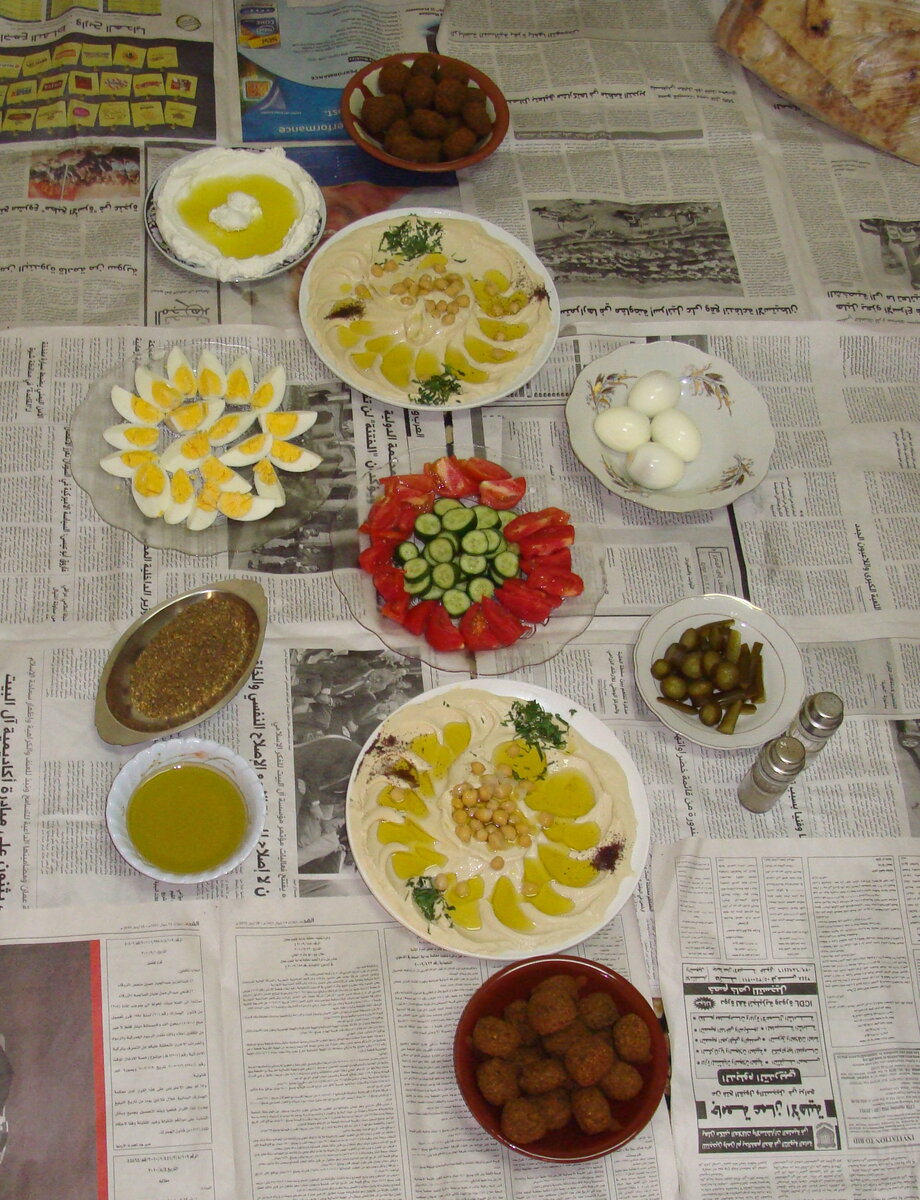 Традиционный обед в арабской семье: хумус, фалафель, оливковое масло, оливки, мягкий сыр (белый в тарелке), яйца, овощи и острый соус (в длинной тарелке слева).
