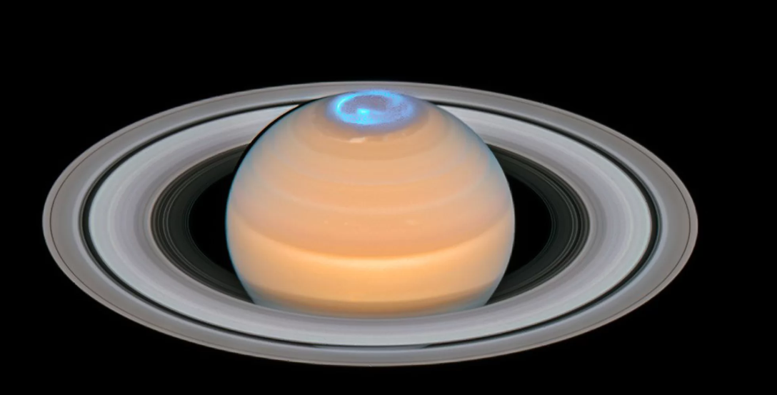 Составное изображение помещает измерения космического телескопа Хаббла ультрафиолетовых полярных сияний Сатурна поверх изображения видимого света планеты. Хаббл измерил полярные сияния Сатурна в течение нескольких месяцев вокруг его Северного солнцестояния, чтобы узнать больше о магнитном поле планеты.