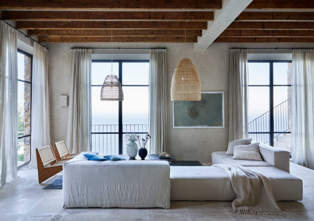 Лаундж-­зона. Модульный диван в льняных чехлах, подушки из винтажных тканей, ан­тиквар­ный датский ковер из конопли, плетеные абажуры и кресла из ротанга — работа More Decor, а в качестве журнального столика дизайнеры приспособили старинную африканскую кровать. В простенке между окнами — работа современного испанского художника Гильема Надаля из Pelaires Gallery. Каше­мировый плед, Frette.