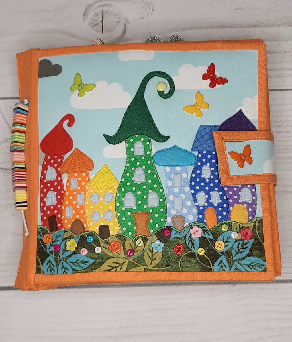 На обложке сказочный город из 7 разноцветных домиков. Как мне кажется, такая картинка отражает тематику книги "Цвета". Книга застегивается на хлястик с помощью магнитной кнопки