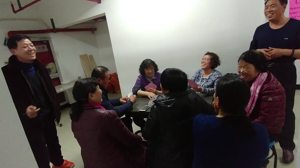 Китайцы играют в карты и запевают песни в помещении для досуга.