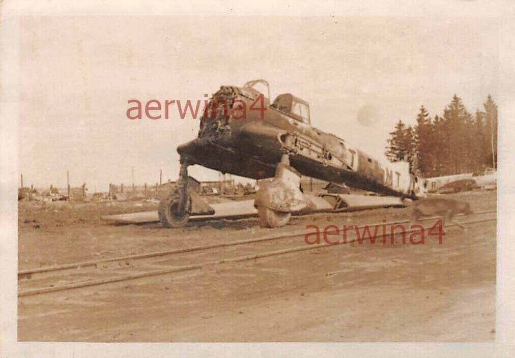 Разбитый Ю-87 "Штука" . Stuka -сокращенное Sturzkampfflugzeug - пикирующий бомбардировщик. Русские названия -лаптёжник и певун, за характерные массивные шасси и вой при пикировании. Видны тактические знаки. Перед самолетом проложены рельсы. Справа убегает из кадра собака. 