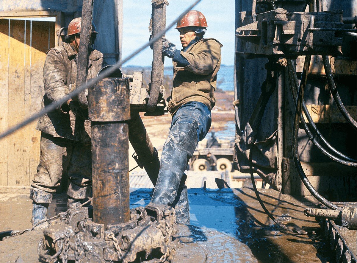 На "серьгах" - лафетный хомут. Кран-блок затащит трубу на площадку, поднимет и установит на муфту трубы. Пневмоключ (справа) захватить сменными "зубами" трубу и навернет на муфту нижней. Клинья (внизу с цепями) на месте.  Потом вертлюг, подача раствора и продолжение бурения. 
  С этого начинался путь многих советских управленцев.