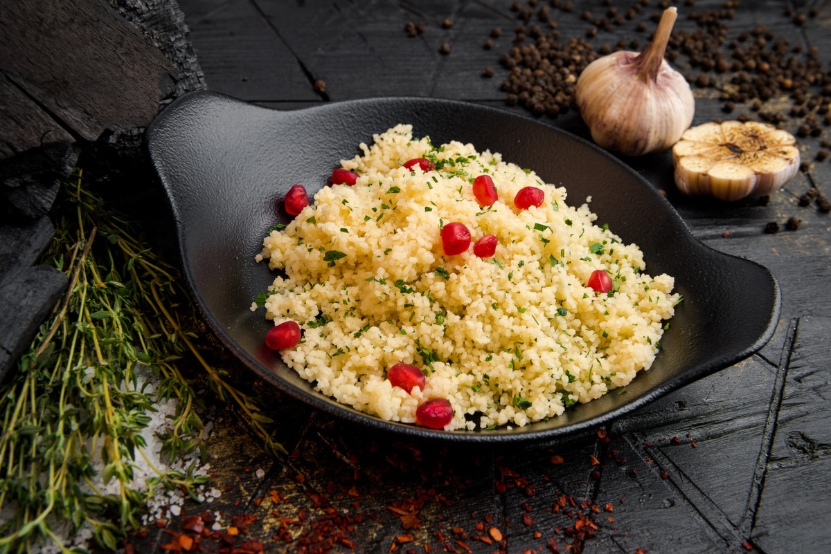 Кускус: что это за крупа Кускус — крупа, которая стала популярна еще в XVIII веке в Северной Африке. Он был основным продуктом в тунисской, ливийской и алжирской кухне. В первоначальном варианте кускус делали из проса, а затем стали использовать манную крупу. Иногда его делают из пшена, ячменя или риса.
Кускус производят определенным образом. Сначала манную крупу сбрызгивают водой, а затем смешивают в единую массу. Из нее получаются небольшие крупинки, которые посыпают сухой манкой или мукой и просеивают.
Однако несколько столетий назад процесс приготовления был более трудоемким. Вначале пшеницу измельчали на жерновах до манных крупинок. Далее их также сбрызгивали водой на широком блюде, посыпали мукой, но процесс скатывания происходил вручную.
Берберские женщины круговыми движениями скатывали манные шарики и сушили их на солнце. Далее гранулы просеивали с помощью мелкого ситечка, остальное отправляли на более крупное сито. Слишком маленькие крупинки повторно обсыпали мукой или манкой — из этого и получался кускус. Эту процедуру женщины проделывали по несколько часов, пока не появилось специальное оборудование и процесс стал автоматизированным.
По вкусу крупа напоминает макароны с легкими ореховыми нотками и ароматом манки. Внешне похожа на рис, но с более мелкими крупинками светло-желтого цвета.