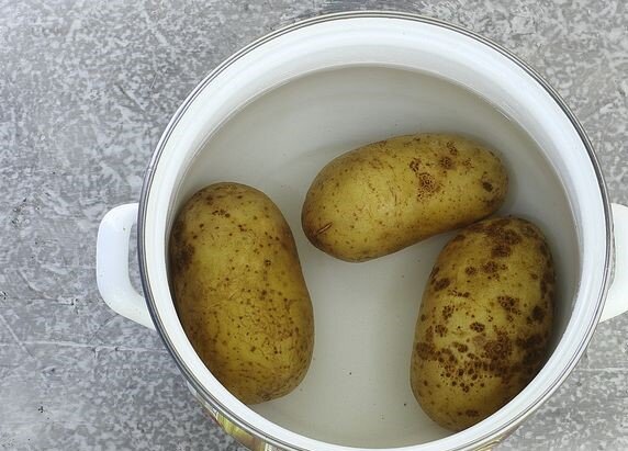 Картофель хорошо вымойте вместе с кожурой. Залейте холодной водой и отправьте на сильный огонь. Немного подсолите картофель и варите 15-25 минут, до готовности. С момента закипания сделайте умеренный огонь. Время варки зависит от сорта и размера картошки. Проколите клубни шпажкой. Если легко прокалываются, значит овощи готовы. Готовый картофель достаньте из отвара и остудите.