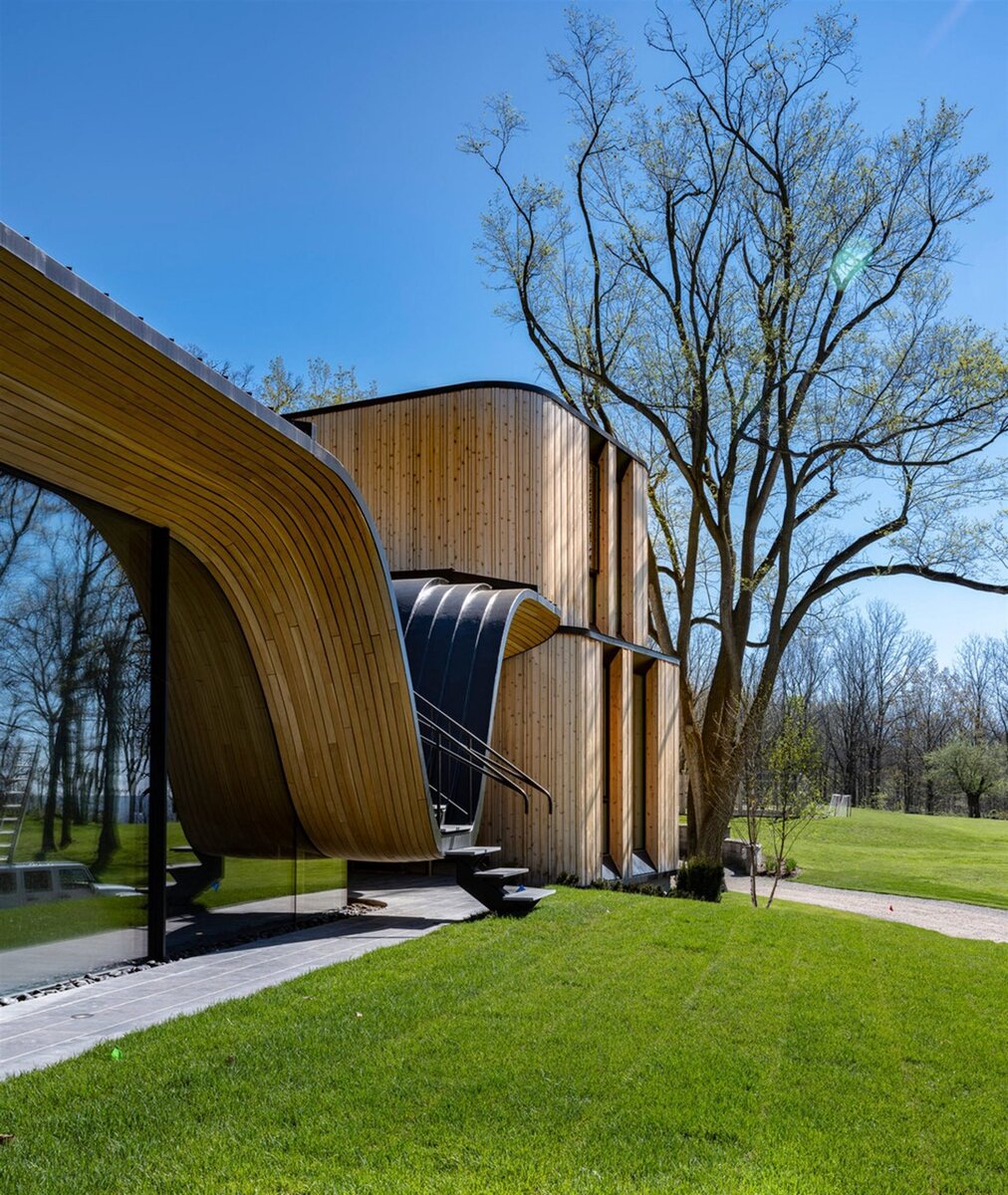 Современный дом с изогнутым деревянным фасадом в лесах Канады
