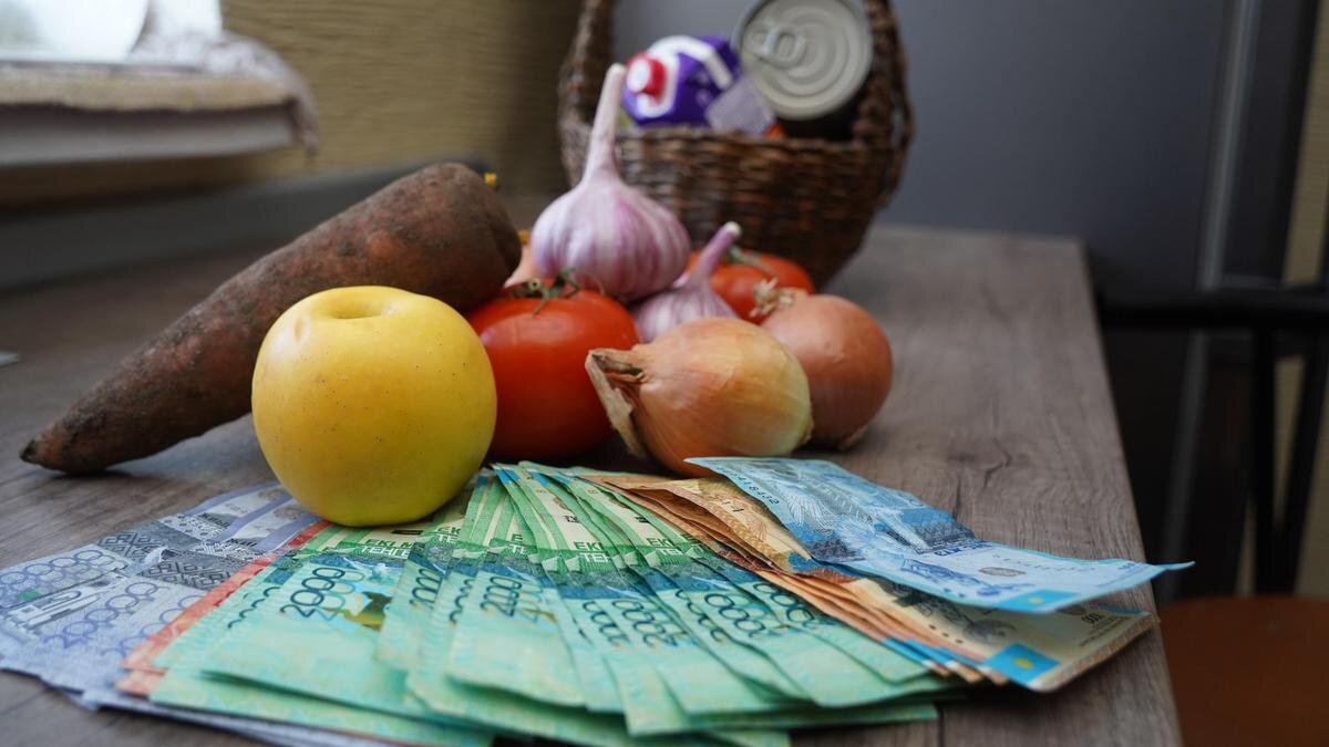    Купюры тенге лежат перед продуктовой корзиной.:NUR.KZ / Владимир Третьяков